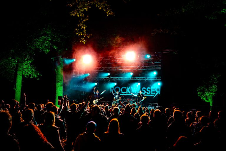 Rockkonzert im Freien bei Nacht mit beleuchteter Bühne.