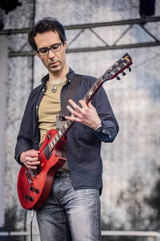 Gitarrist spielt auf Bühne mit roter E-Gitarre.