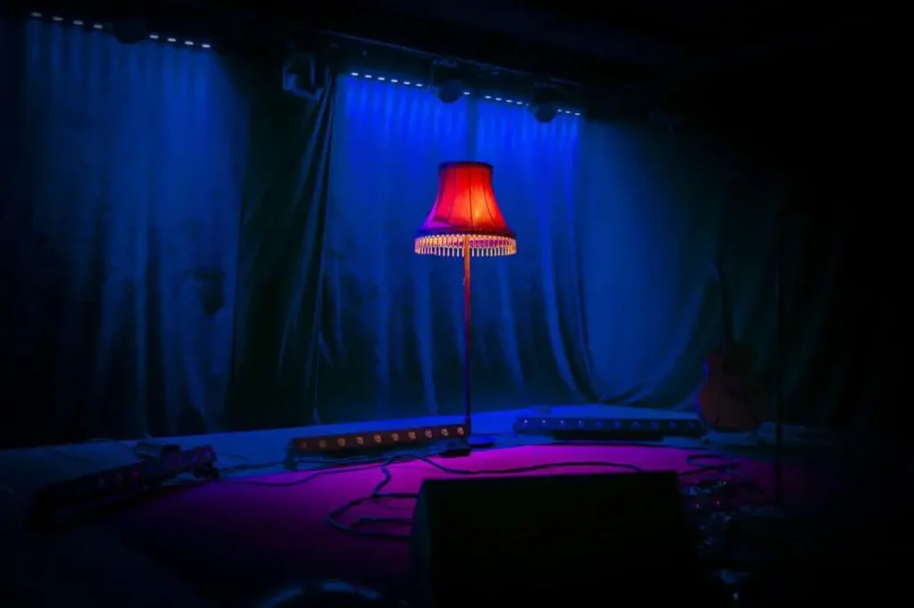 Beleuchtete Stehlampe auf dunkler Bühne mit Gitarre.