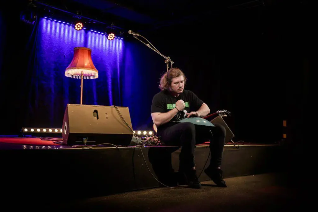 Musiker spielt Handpan auf Bühne mit roter Lampe.
