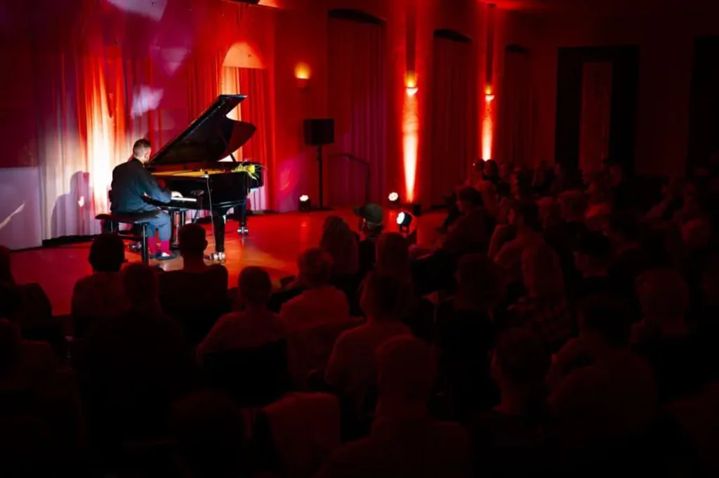 Pianist spielt vor Publikum im beleuchteten Saal.
