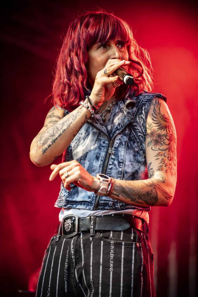Sängerin mit Tattoos performt auf Bühne vor rotem Hintergrund.