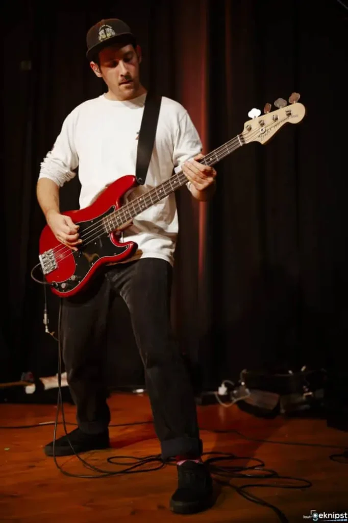Mann spielt rote Bassgitarre auf Bühne.