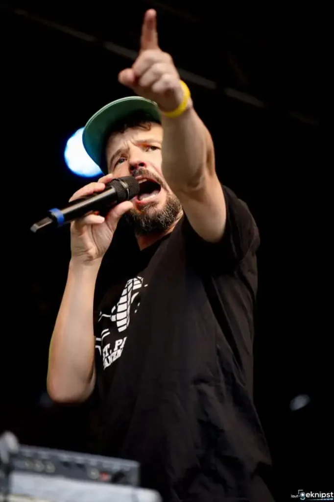 Rapper mit Mikrofon hebt Finger auf Bühne.