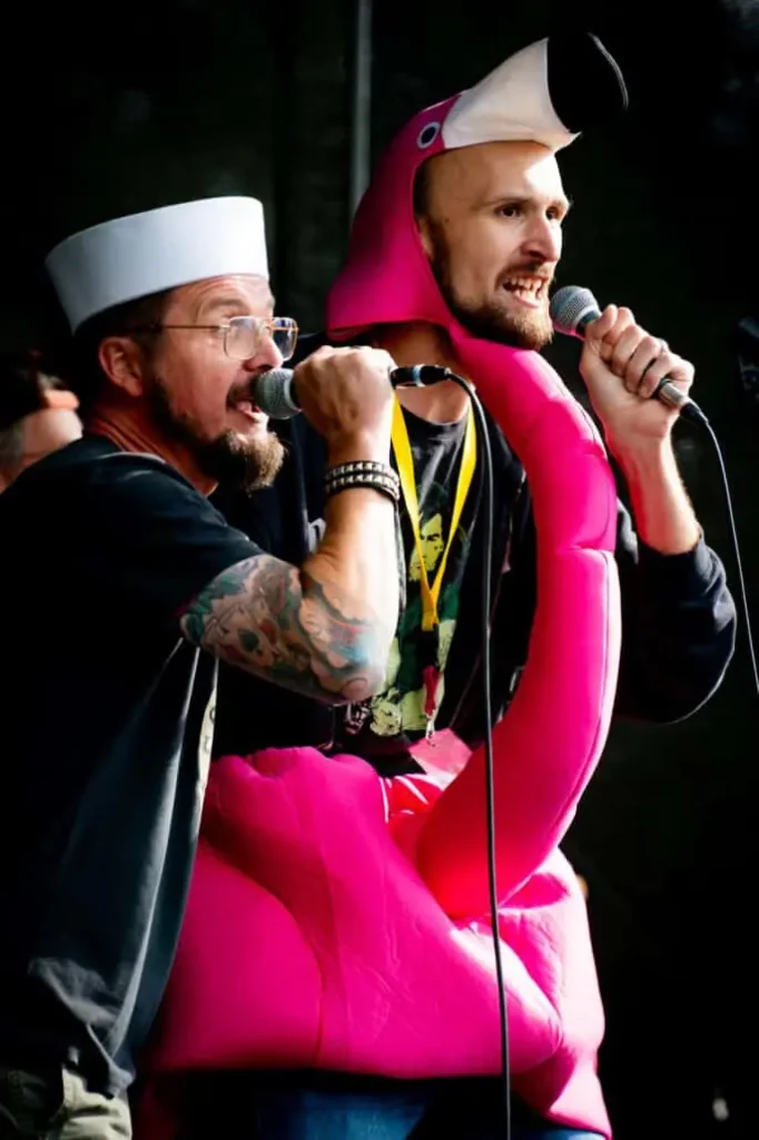 Männer singen auf Bühne in Flamingo-Kostüm und Matrosenhut.
