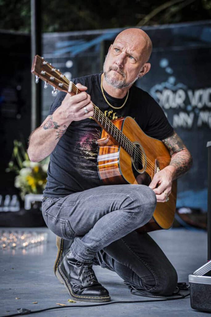 Glatzköpfiger Mann spielt akustische Gitarre.