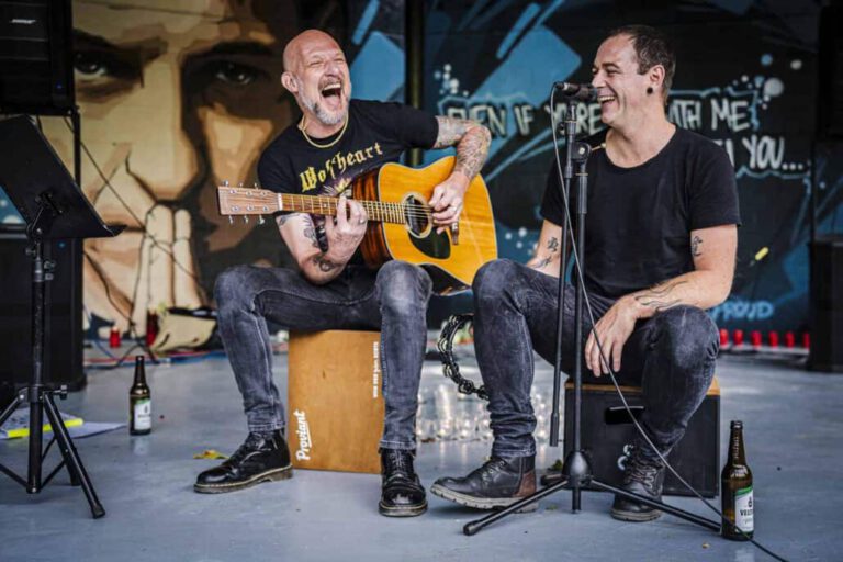 Zwei Gitarristen lachen und spielen live.