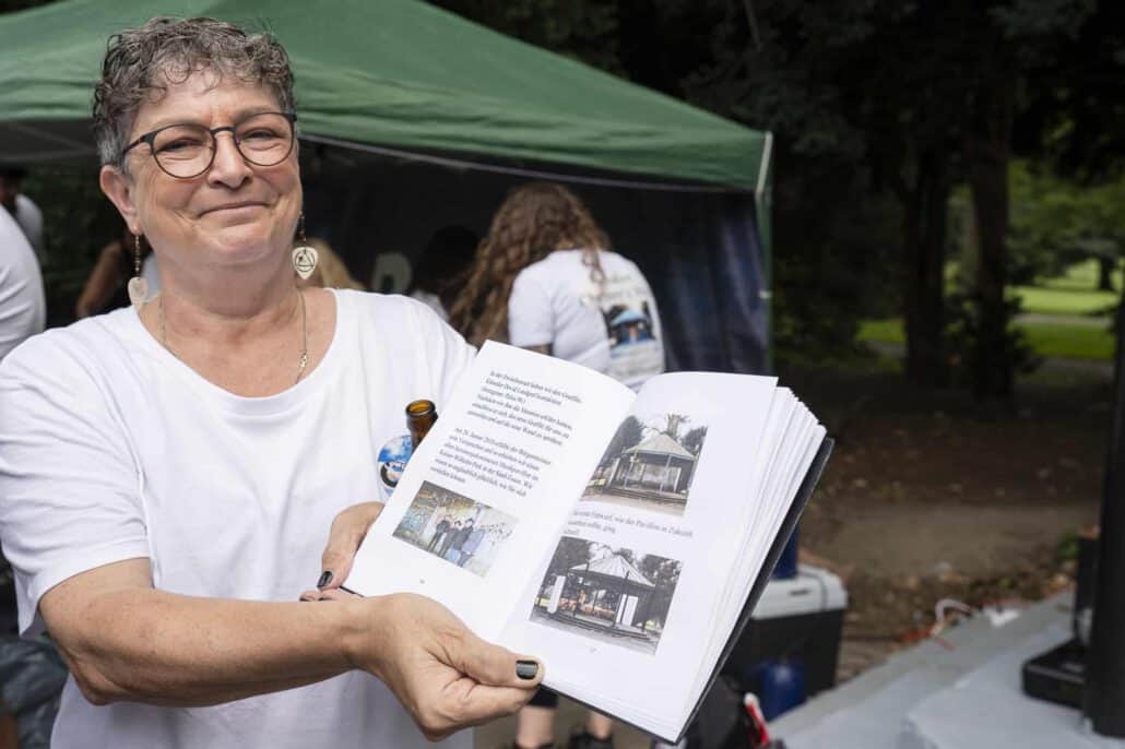 Frau zeigt Broschüre bei Veranstaltung im Park.