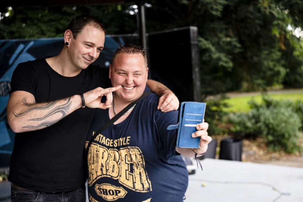 Zwei Männer lächeln und posieren mit Smartphone.