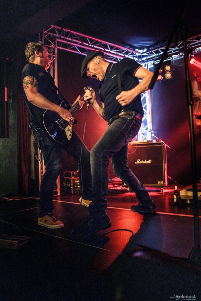 Zwei Gitarristen rocken energisch auf Bühne.