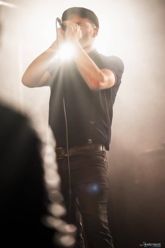 Sänger mit Mikrofon im Scheinwerferlicht auf Bühne.