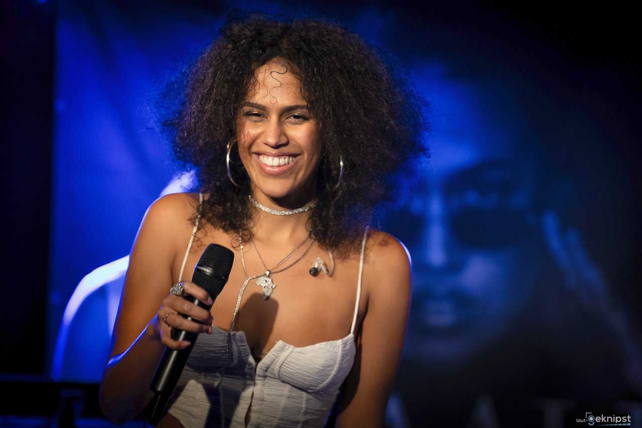 Sängerin mit Mikrofon lacht auf Bühne.