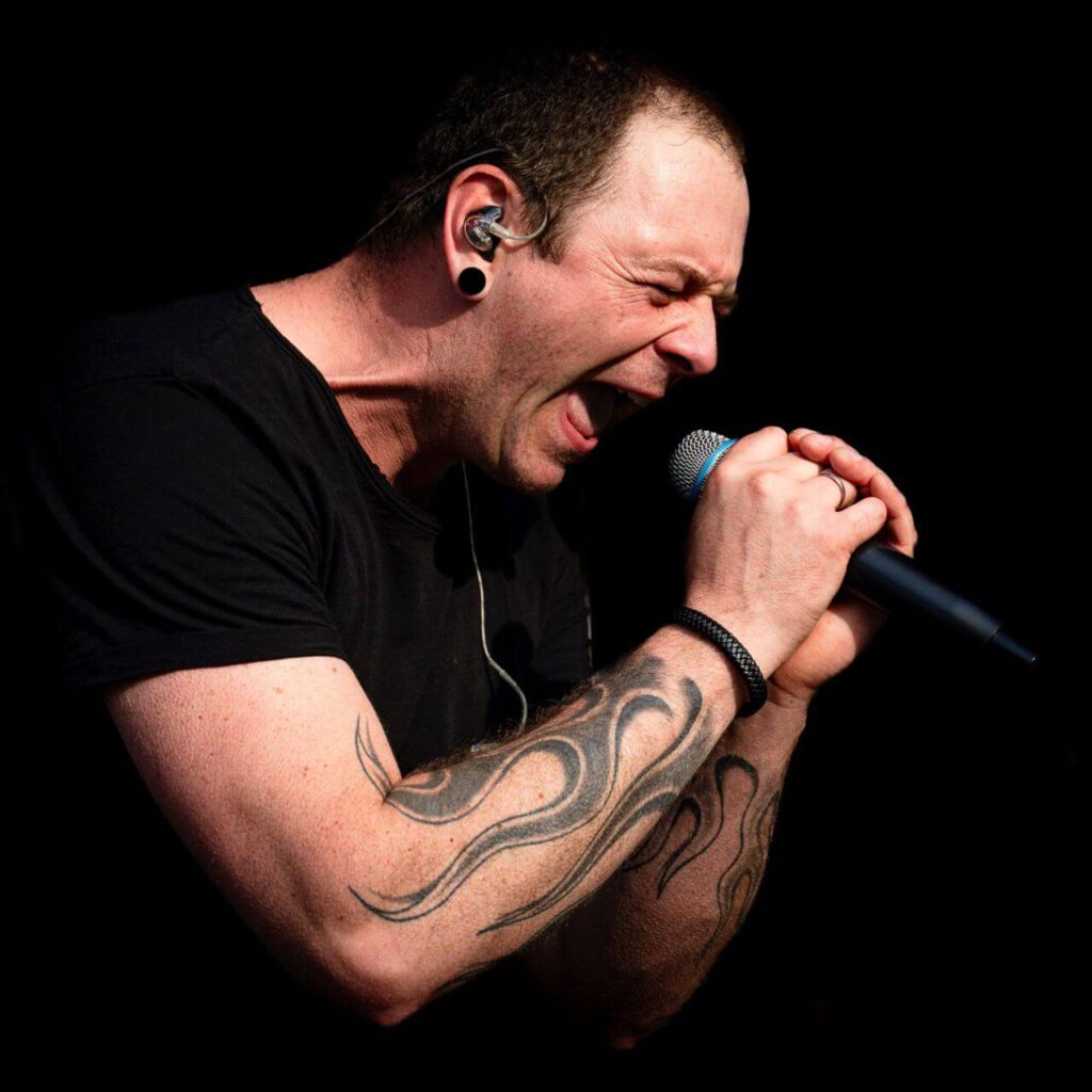 Sänger mit Tattoo singt leidenschaftlich ins Mikrofon.