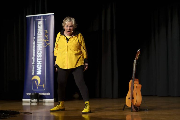 Frau singt laut auf Bühne neben Gitarre.
