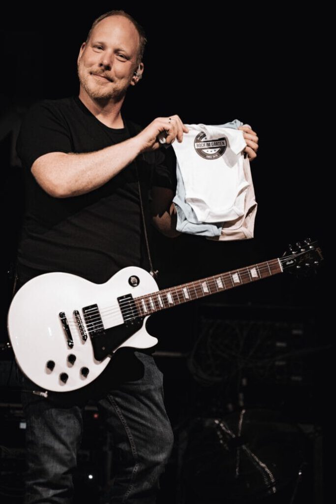 Gitarrist präsentiert Shirt auf Konzertbühne.