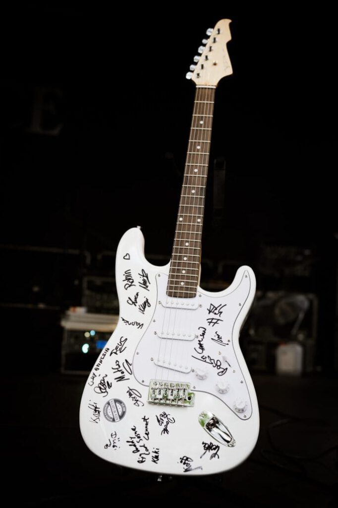 Weiße E-Gitarre mit vielen Autogrammen darauf.