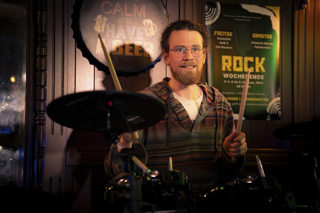 Schlagzeuger lächelt in Bar mit Neonlichtern.
