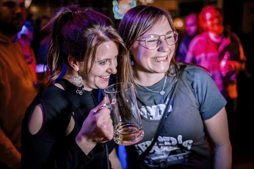 Zwei Freundinnen lachen mit Bierglas auf Party.