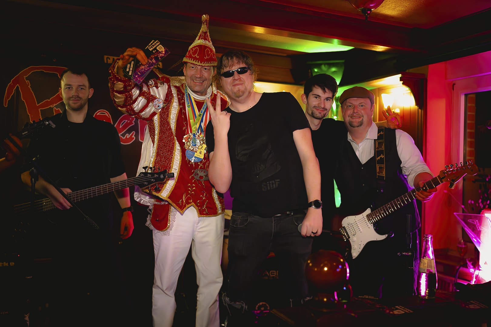 Band posiert mit Karnevalskönig auf Bühne.