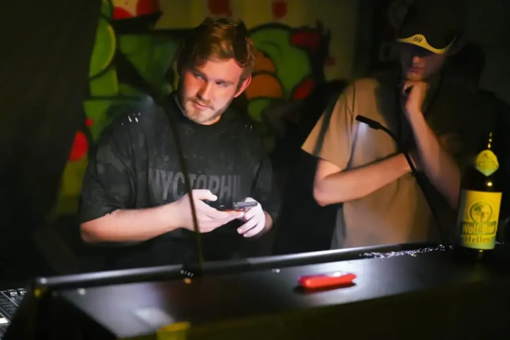 DJ nutzt Smartphone an beleuchtetem Mischpult.