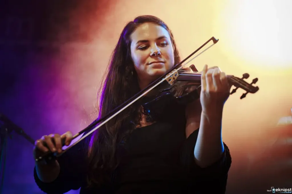 Frau spielt Geige auf Bühne mit farbigem Licht.