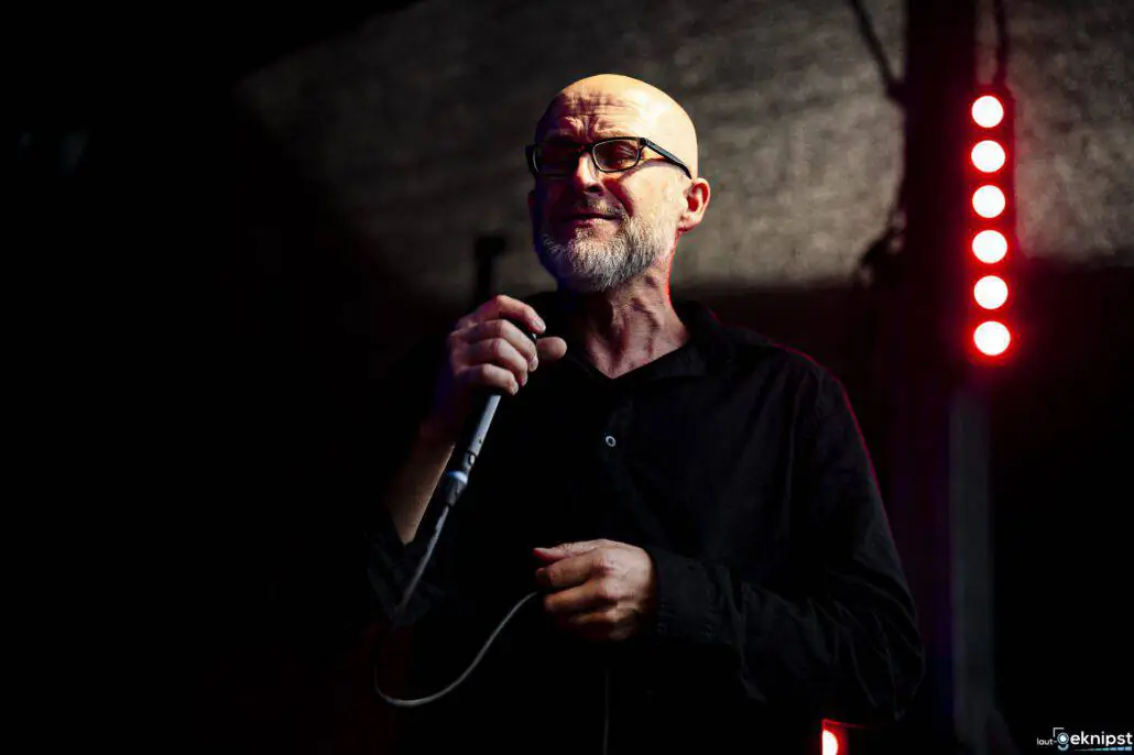 Glatzköpfiger Mann singt in Mikrofon auf Bühne.