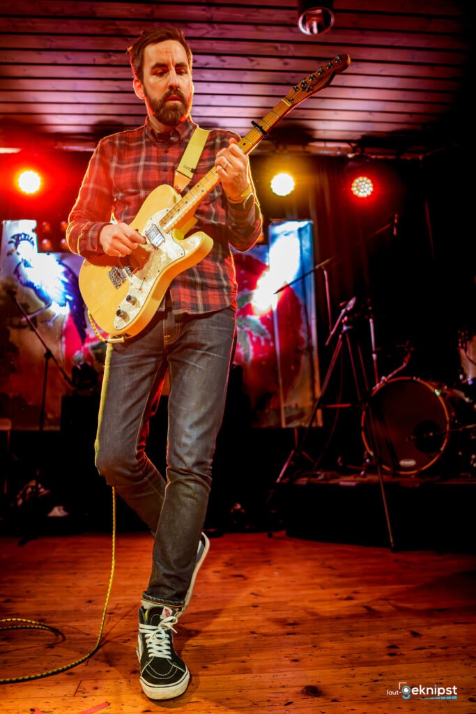 Musiker spielt Gitarre auf der Bühne, bunte Lichter.