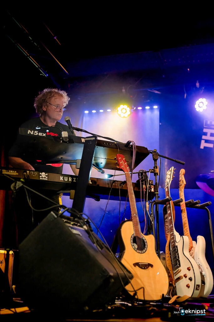 Musiker spielt Keyboard auf einer Bühne mit Gitarren.