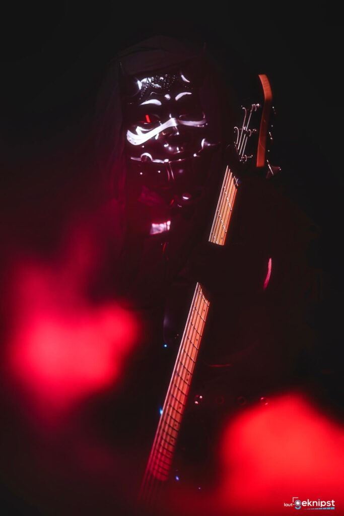 Musiker in dämonischer Maske mit Gitarre, rotes Licht.