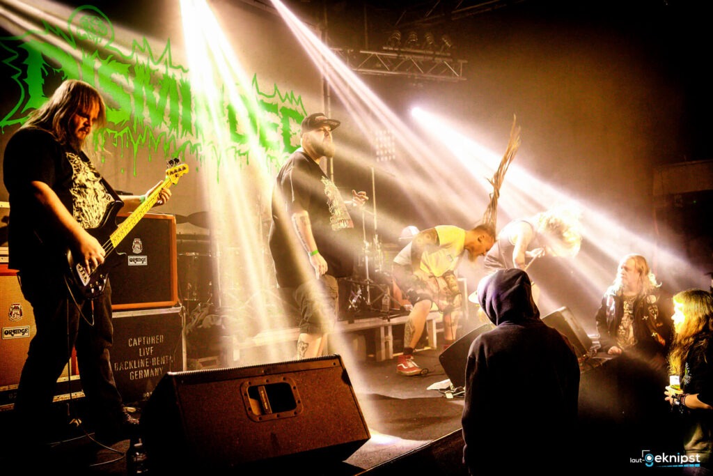 Metalband spielt live auf heller Bühne.