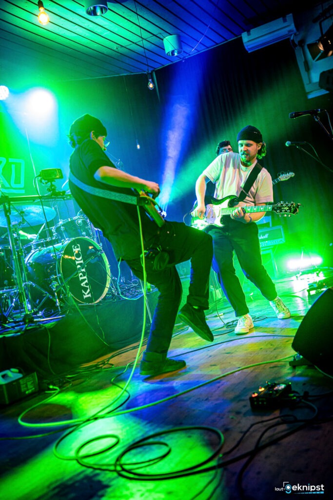 Zwei Musiker spielen Gitarren auf Bühne mit Lichteffekten.