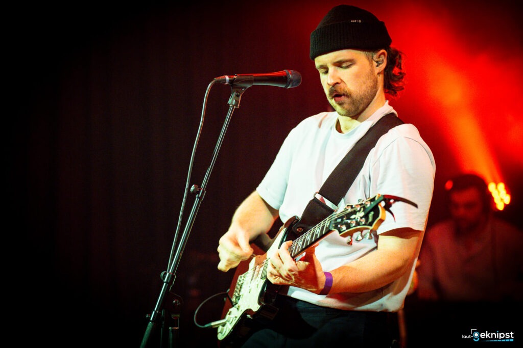 Person spielt Gitarre auf der Bühne, rotes Licht.