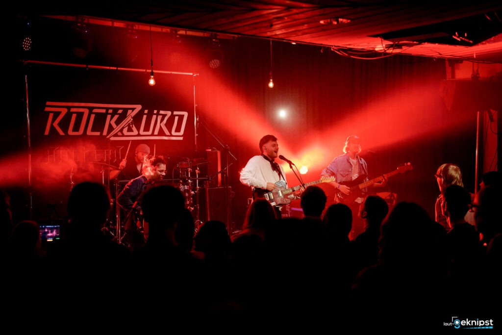 Band spielt Live-Konzert, beleuchtet in rotem Licht.