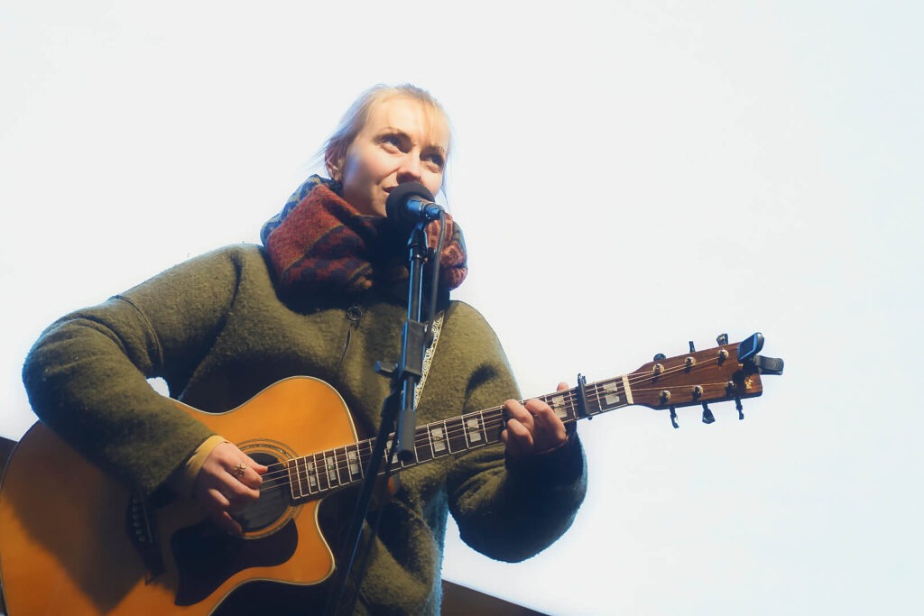 Person spielt Gitarre und singt ins Mikrofon.