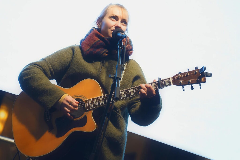 Frau singt und spielt Gitarre auf Bühne.