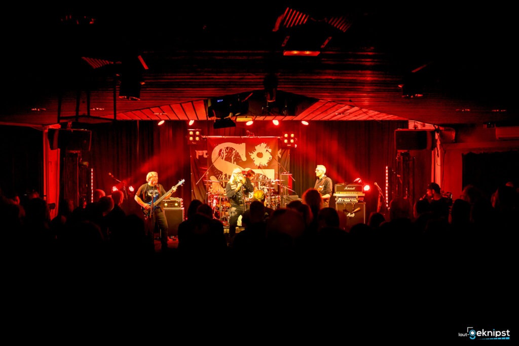 Liveband auf roter Bühne performt vor Publikum.