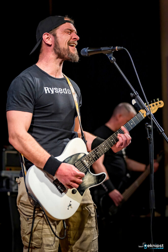 Gitarrist singt auf der Bühne mit Band.