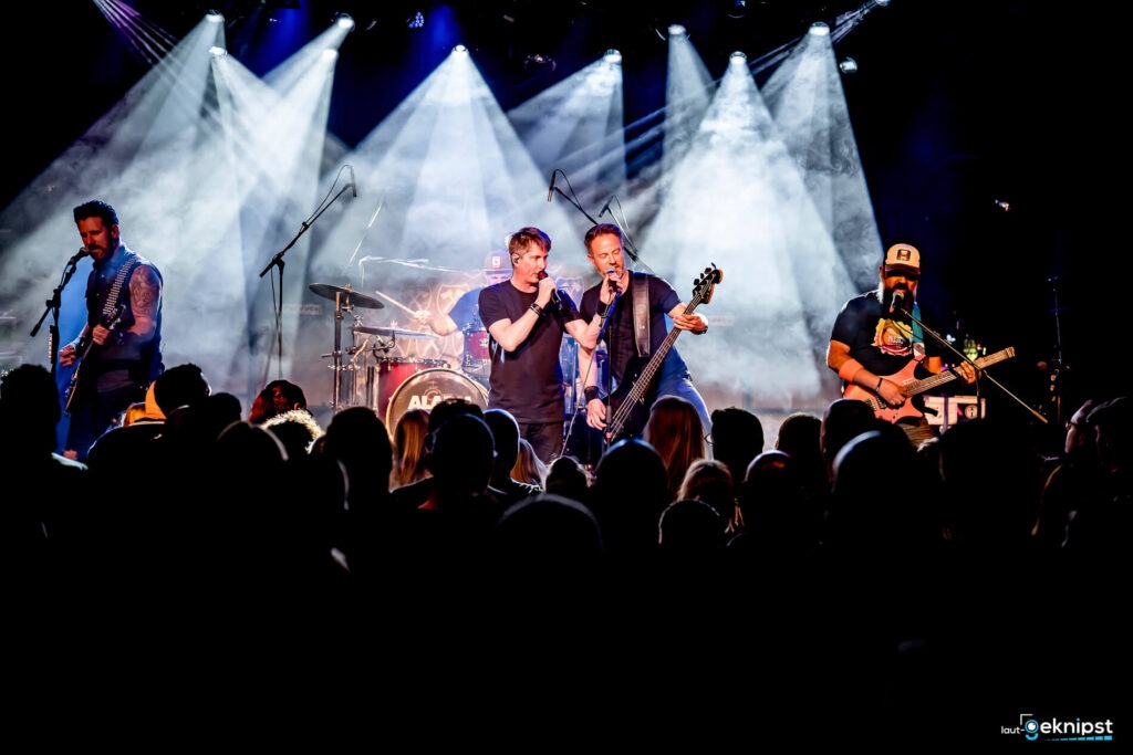 Band spielt auf einer Bühne mit Lichteffekten.