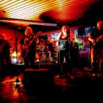 Rockband spielt auf Bühne in rotem Licht.