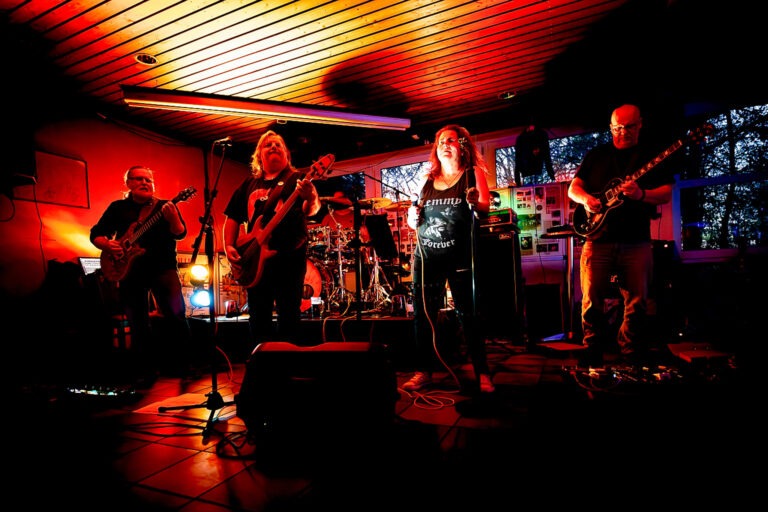 Rockband spielt auf Bühne in rotem Licht.