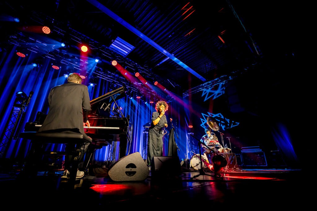 Jazztrio performt auf bühne mit bunten Lichtern.