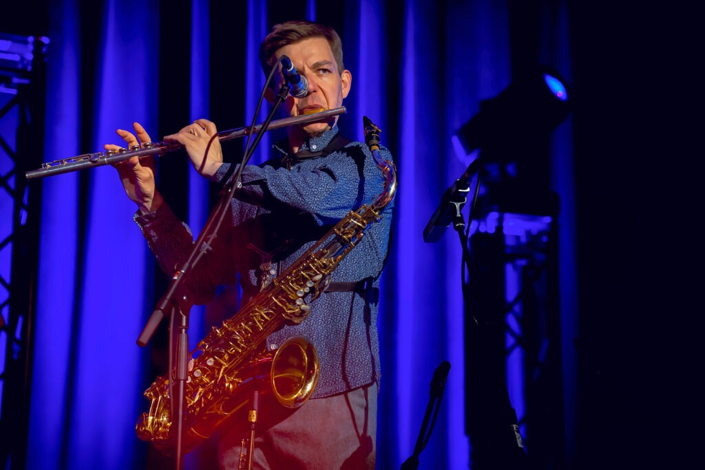 Musiker spielt Flöte und Saxophon auf Bühne.