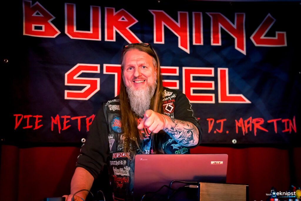 DJ vor Burning Steel-Banner mit ausgestrecktem Arm.