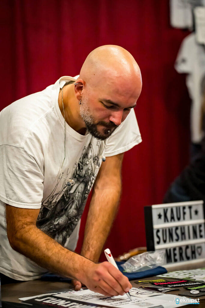 Mann schreibt Autogramme am Merch-Stand.