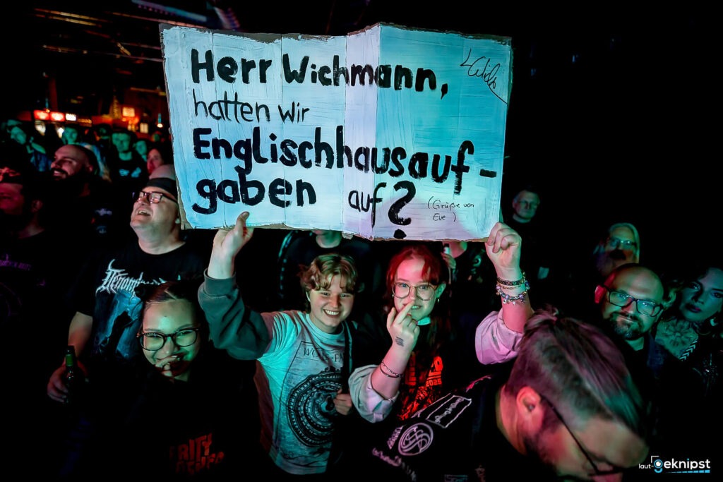 Publikum hält beschriftetes Schild bei Konzert hoch.