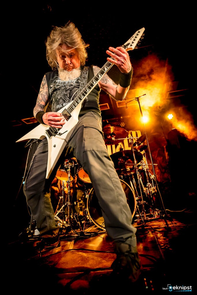 Gitarrist spielt energisch auf der Bühne, gelbe Lichter.