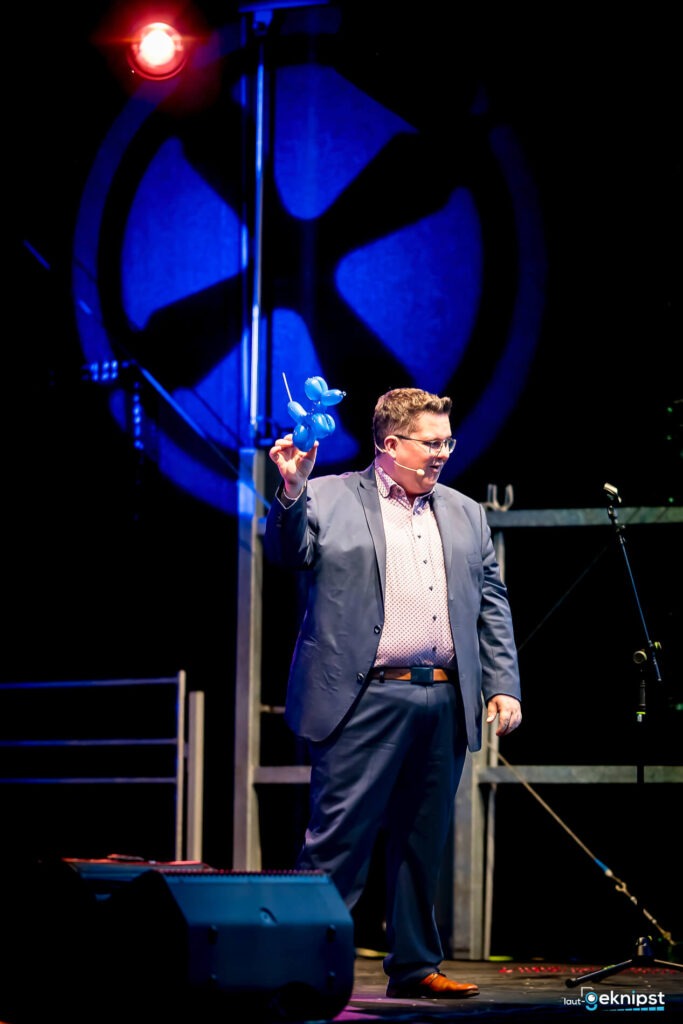 Mann mit blauer Luftballonfigur auf Bühne