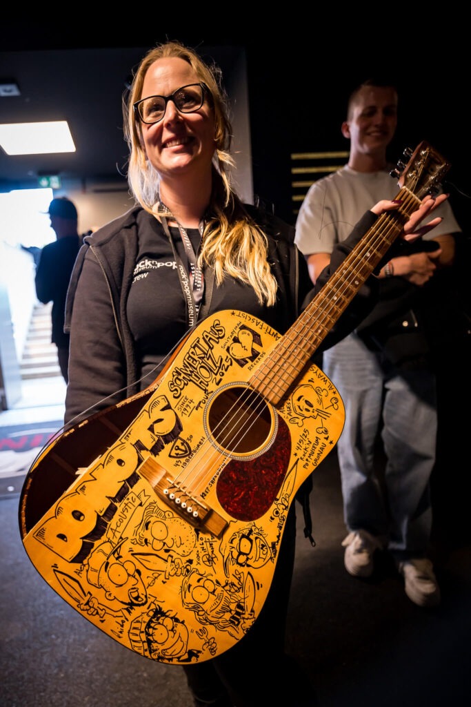 Frau mit signierter, dekorierter Gitarre lächelt freudig.