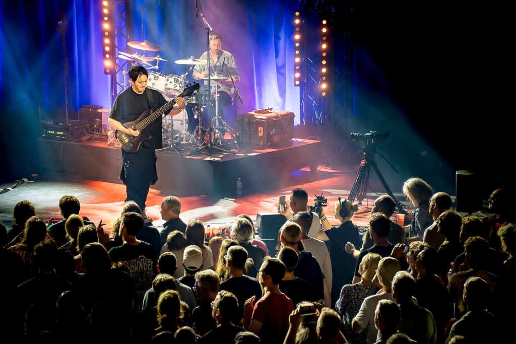 Konzert: Bassist auf der Bühne, Publikum schaut zu.