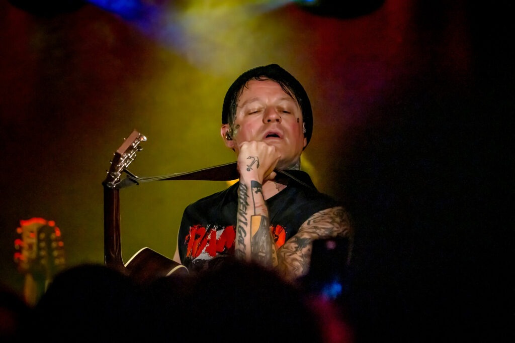 Musiker mit Gitarre auf der Bühne, bunte Beleuchtung.